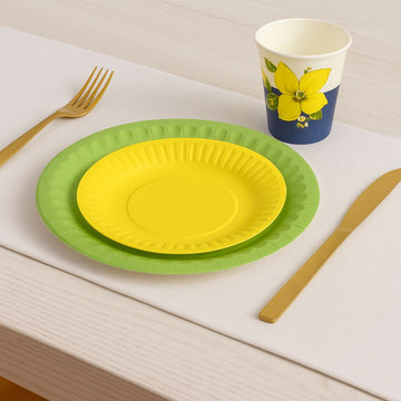 Piatti di carta colorati monouso. Uno grande verde ed uno piu piccolo giallo, Apparecchiati su una tavola con coltello forchetta e bicchiere anch'essi monouso